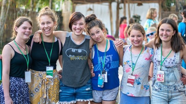 Six teen girls with their arms around each other, laughing together