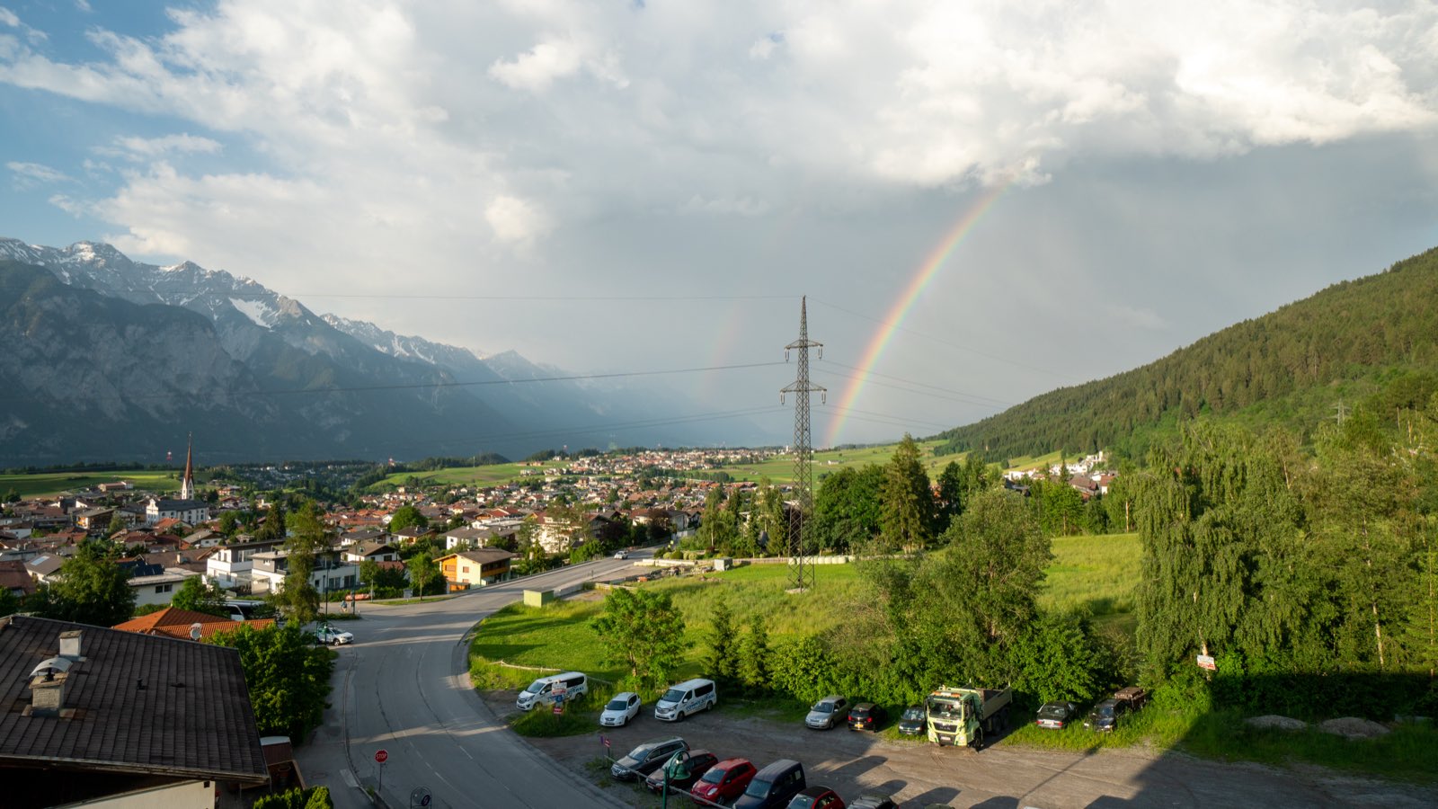 A double rainbow arching over the same green valley and village after an evening rain
