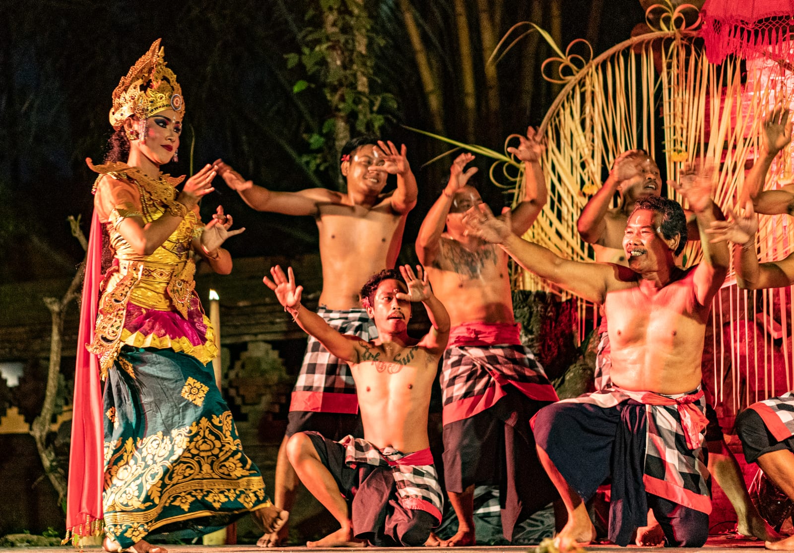 A costumed Balinese dancer and performers lit up on stage at night