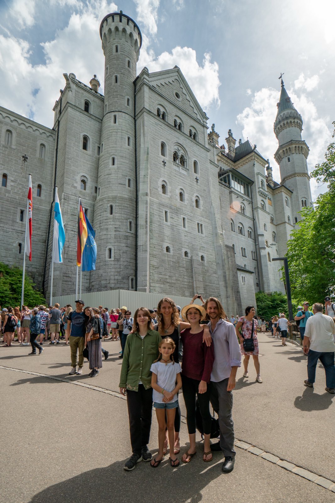 The five of us standing at the foot of Neuschwanstein's towering white walls, flags flying beside the entrance