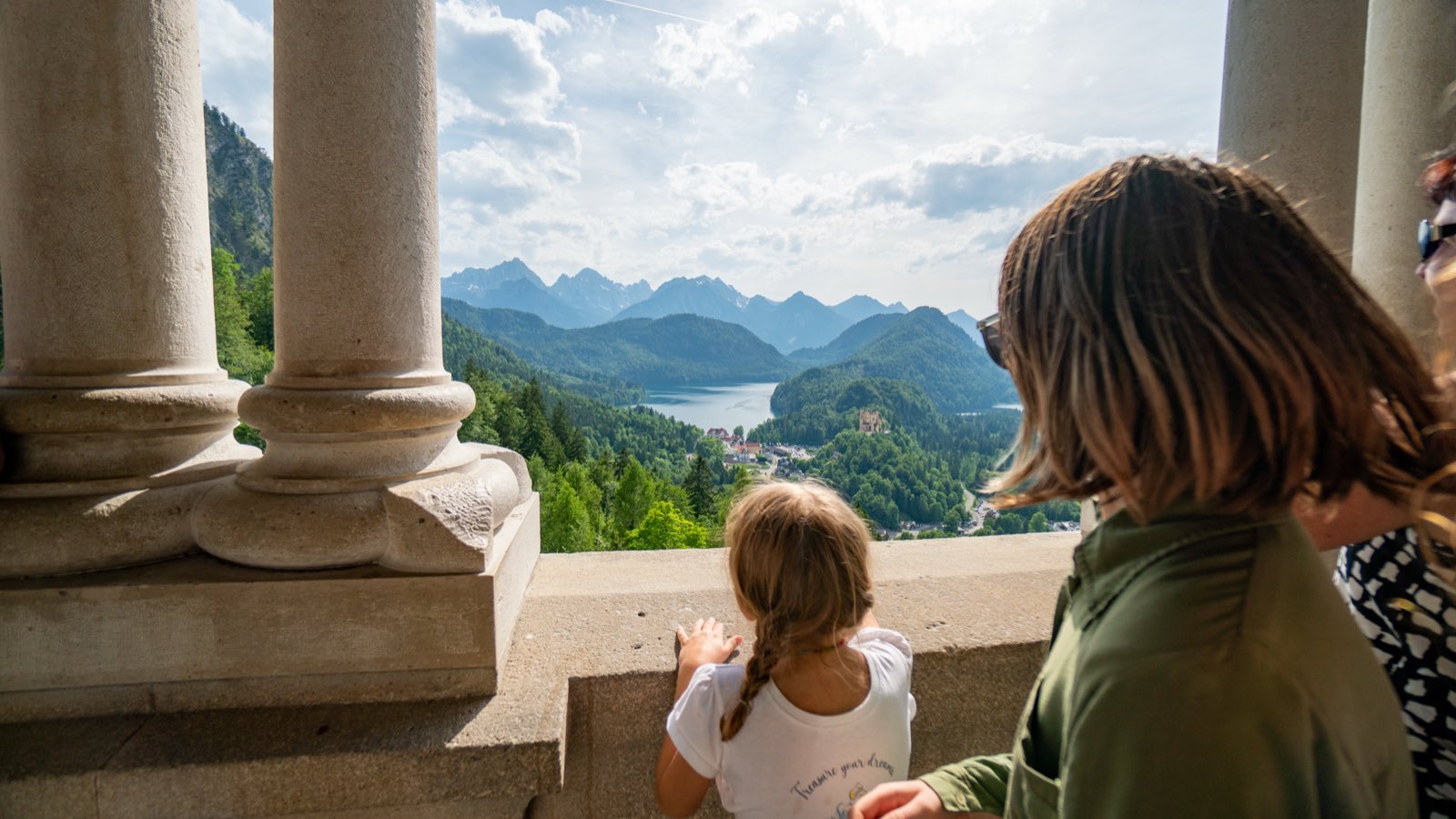 Two of the girls leaning on a stone balustrade, looking out through columns to the lake and mountains far below
