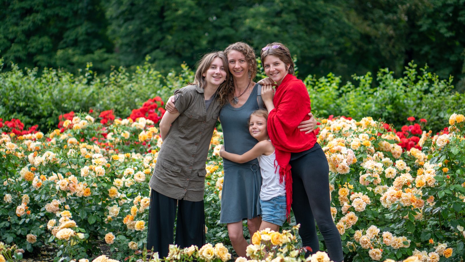 Jennifer and the three girls hugging among beds of red and yellow roses in full bloom