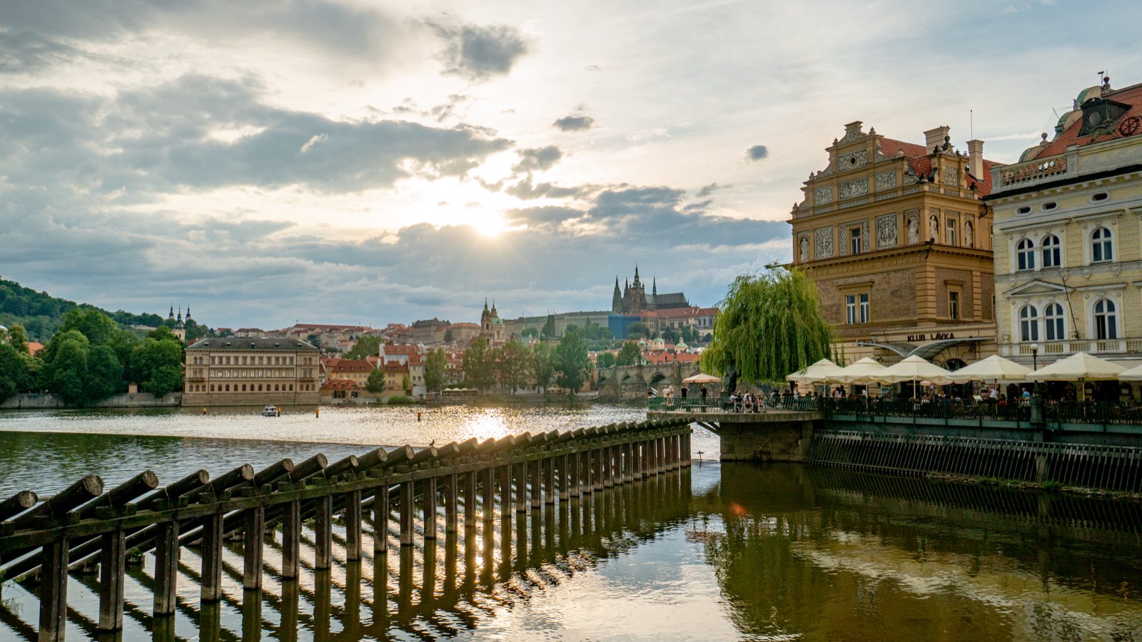 Golden evening light over the Vltava river, Prague Castle and St. Vitus Cathedral on the hill above riverside cafés