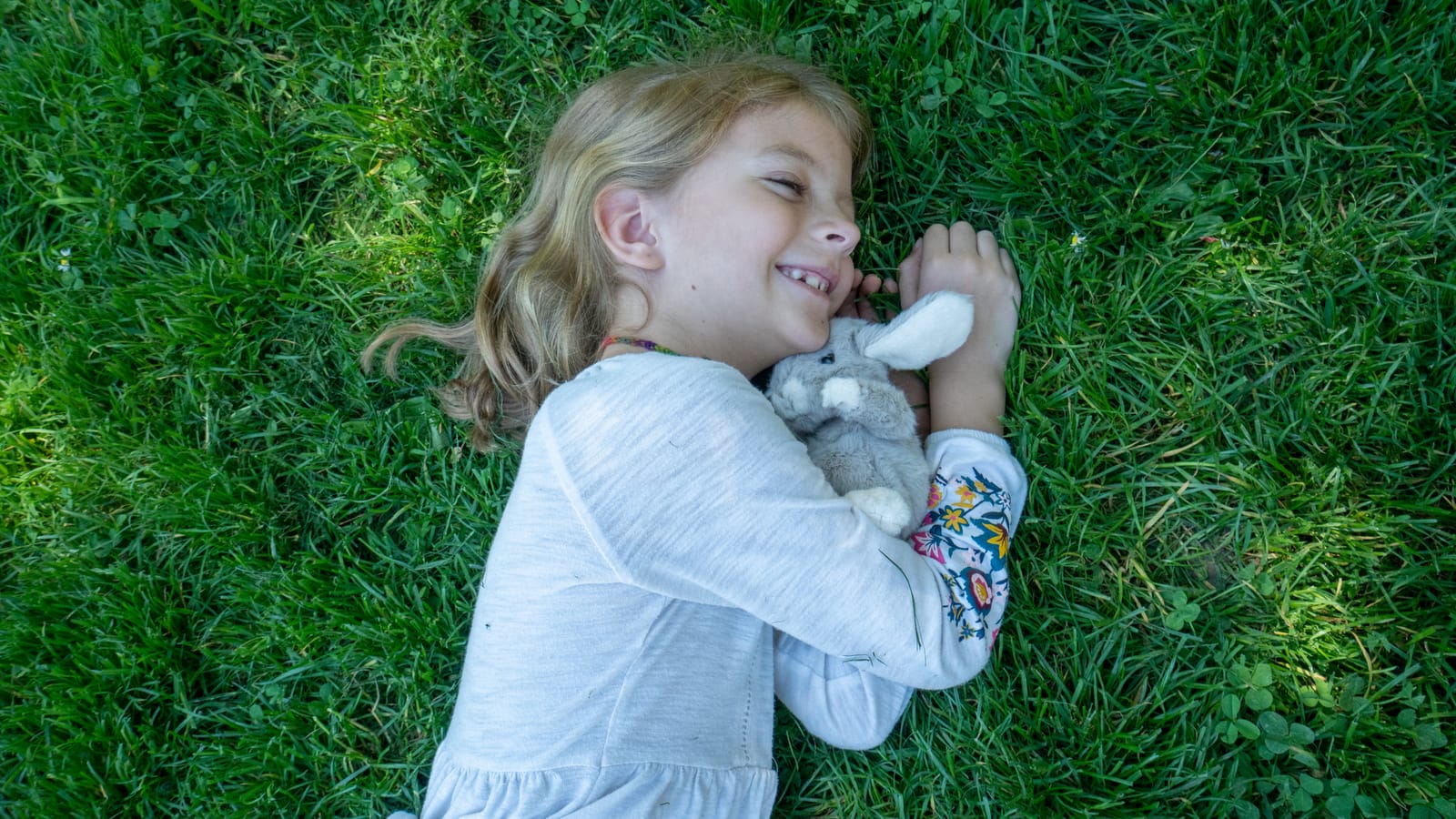 Aysia lying in the grass, cuddling the little stuffed bunny she found in Rothenburg