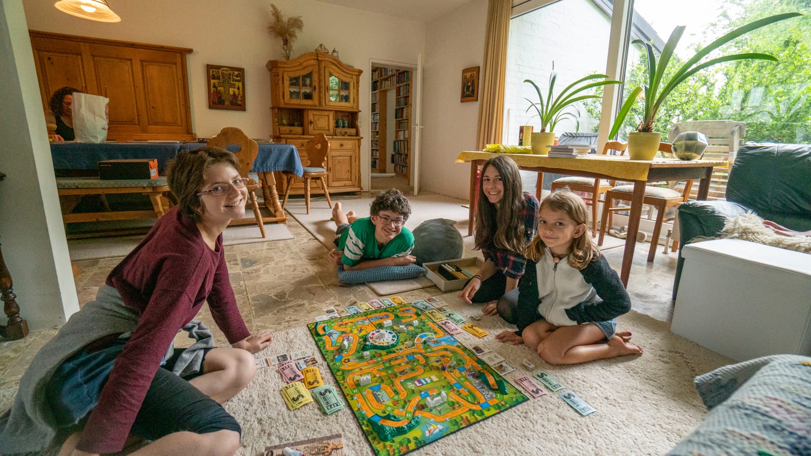 Kids spread out on the floor around a colorful board game in a sunlit living room